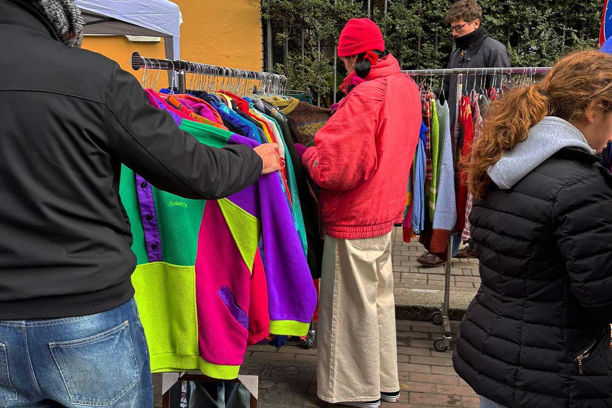 Persone che curiosano tra le giacche vintage colorate appese ai banchi del mercatino Le Pulci Pettinate a Milano