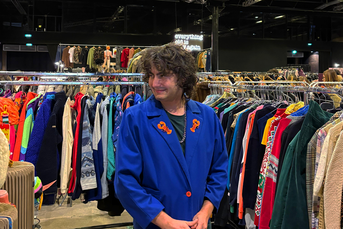 Ragazzo con giacca vintage blu decorata con aragoste rosse ricamate tra i banchi dell East Market di Milano